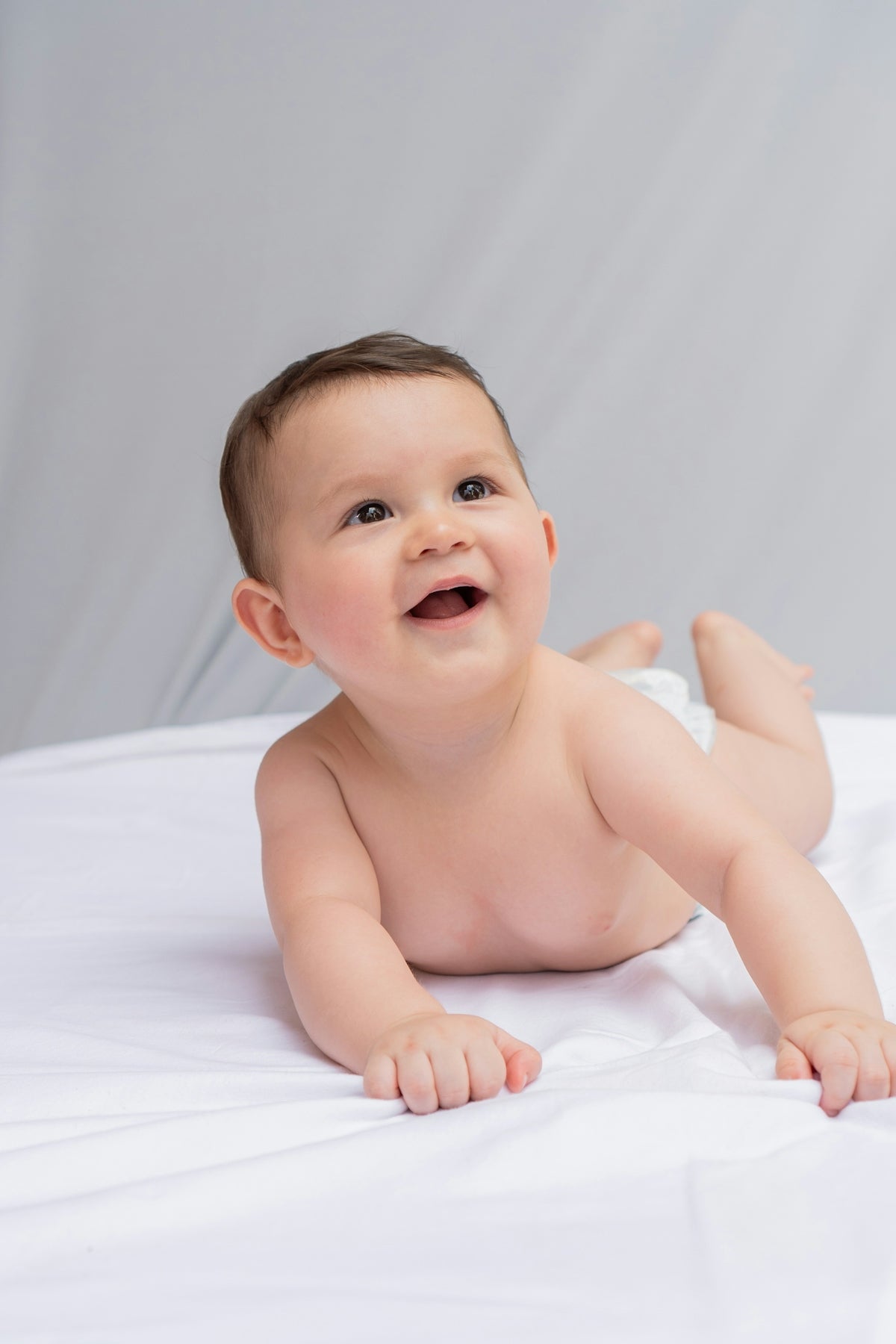 A smiling baby laying on a white sheet