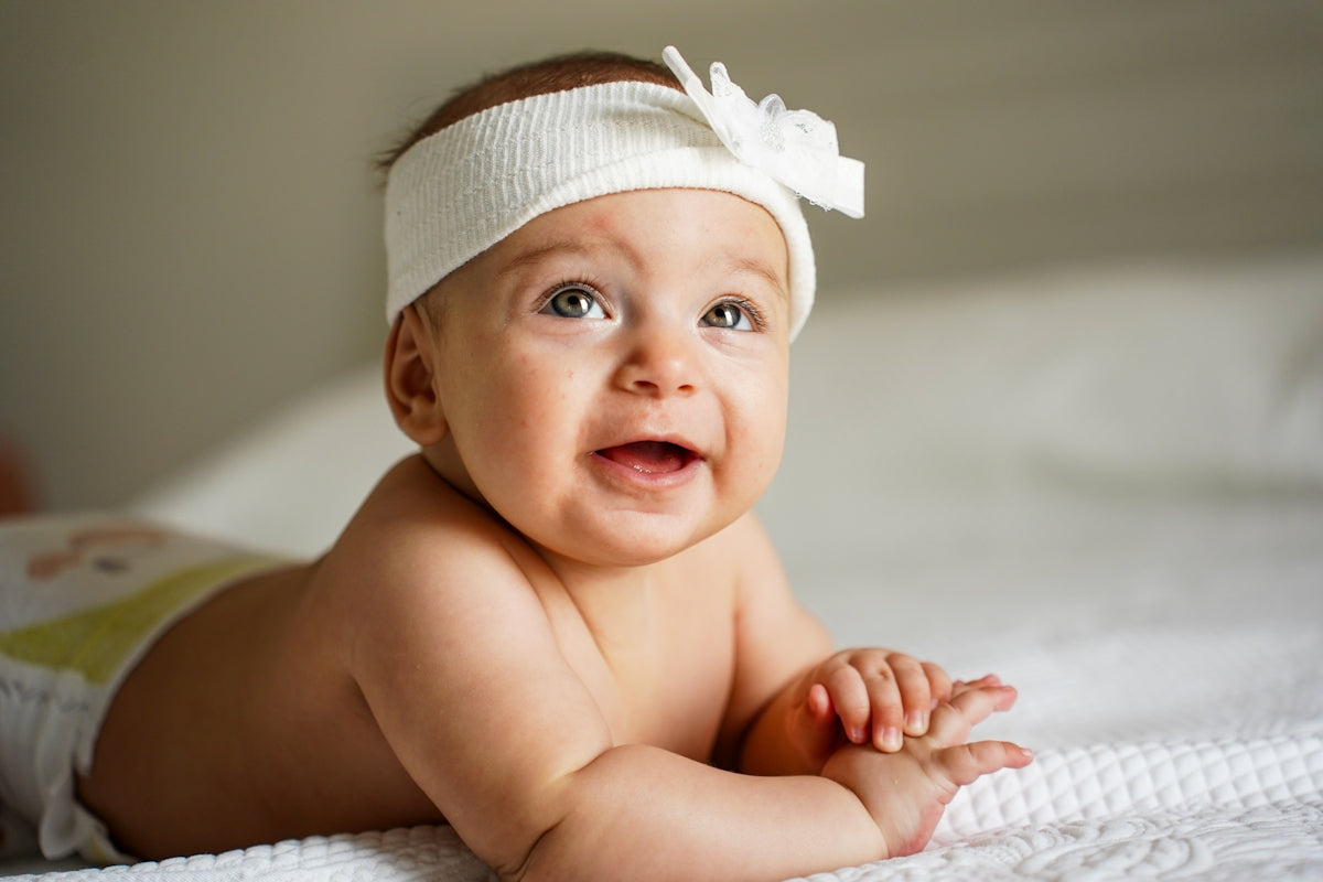 A baby girl wearing a white headband smiles.